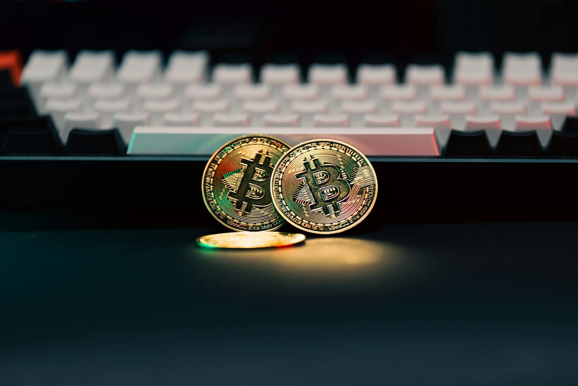 Złote monety z symbolem Bitcoina leżące przed klawiaturą laptopa